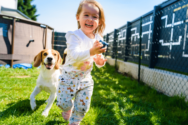 Puppy running with child in a fenced in yard.